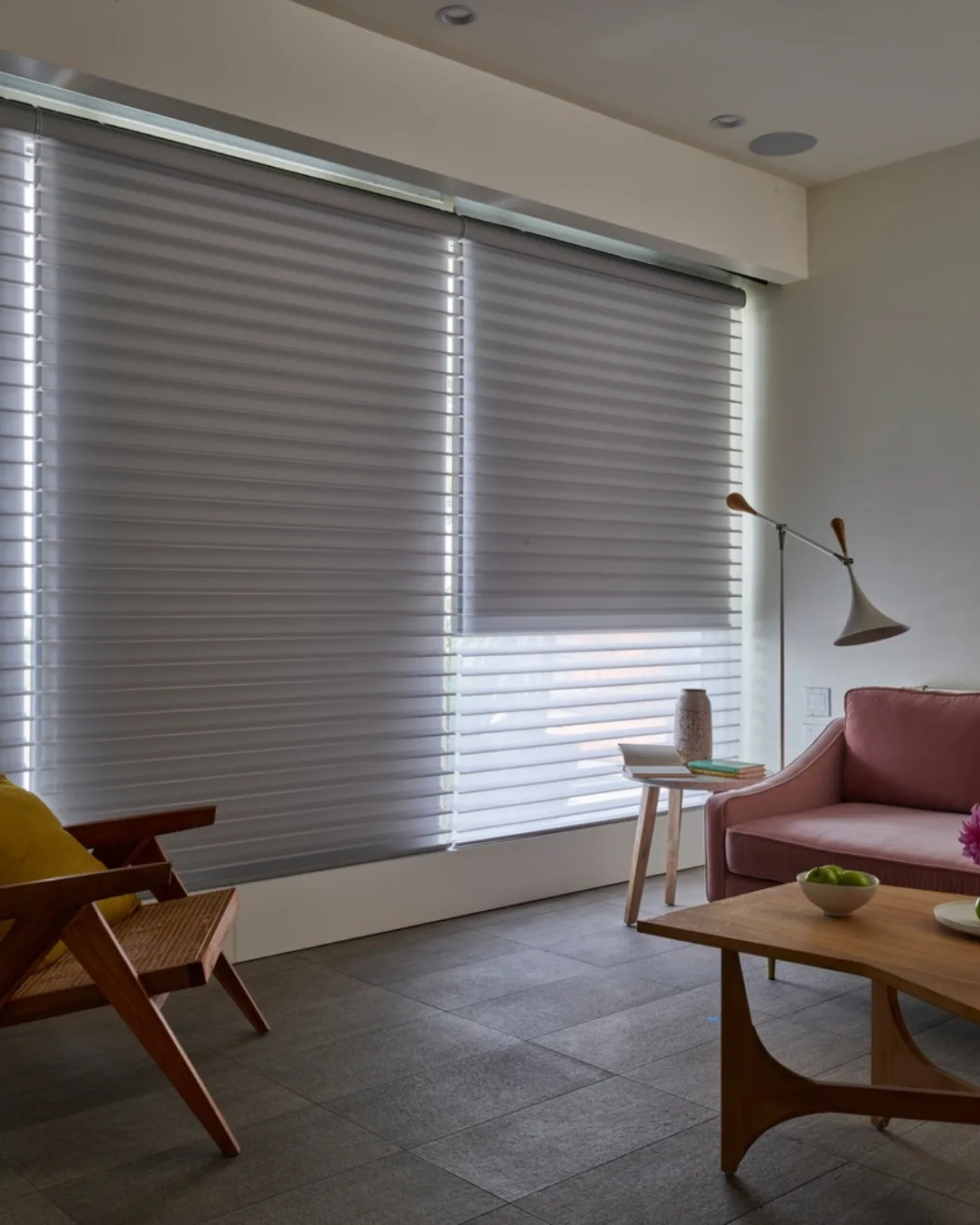 Living room with large window blinds drawn, pink sofa, and wooden coffee table.